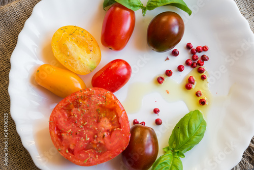 Mixed tomatoes of different colours with herbs and oil on white plate