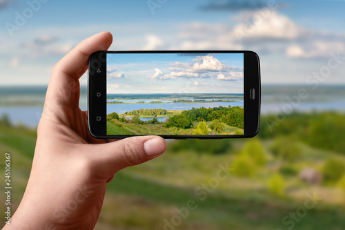Smartphone in hand photographs nature on the screen. Photos of the scenery of the evening river.