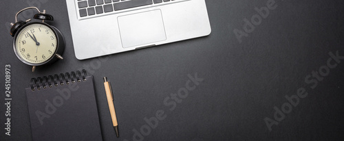 Fotografi Computer laptop and alarm clock on black color office desk, top view