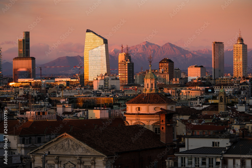 Milan skyline with skyscrapers at sunset. Aerial view of Milano city, Italy. The Grigne mountain range (Lombardy Alps) in the background. Italian landscape panorama.