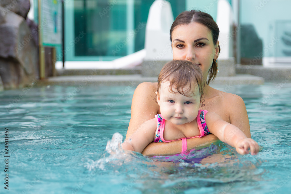 Happy mother teaches to swim daughter in pool against a background of coconut trees