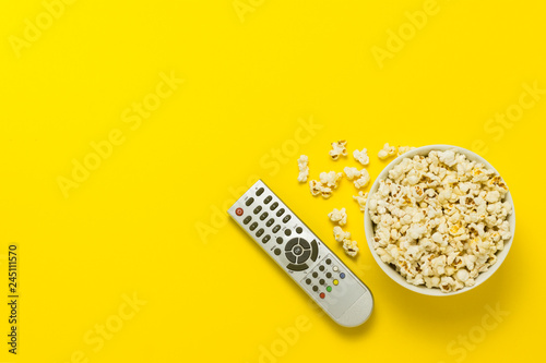 A bowl of popcorn and TV remote on a yellow background. The concept of watching TV, film, TV series, sports, shows. Flat lay, top view