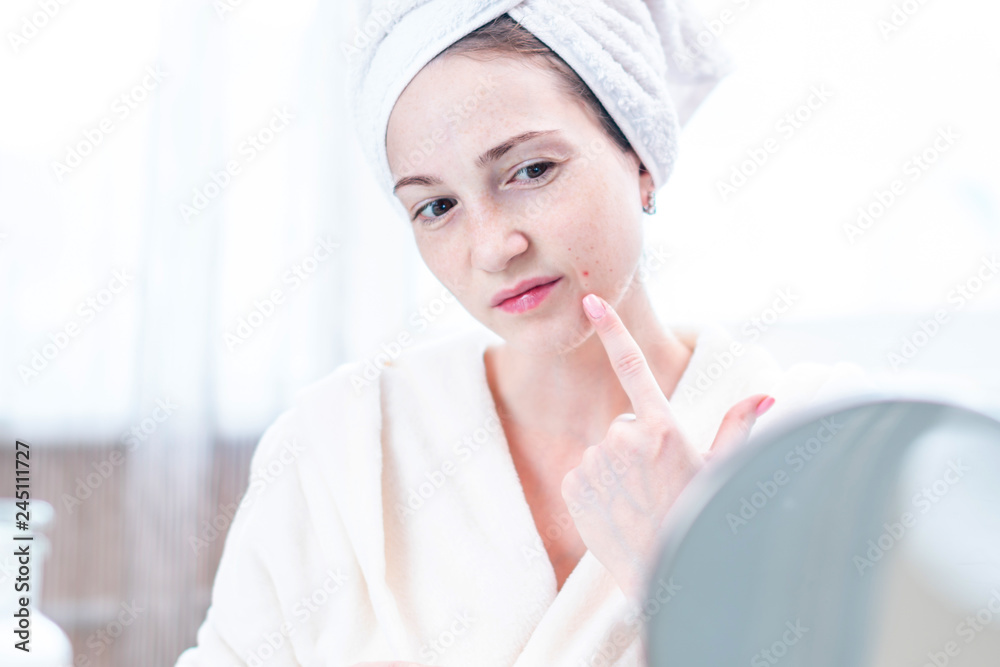 Beautiful unhappy young woman detects acne on her face. Concept of hygiene and care for the skin Beautiful unhappy young woman detects acne on her face. Concept of hygiene and care for the skin