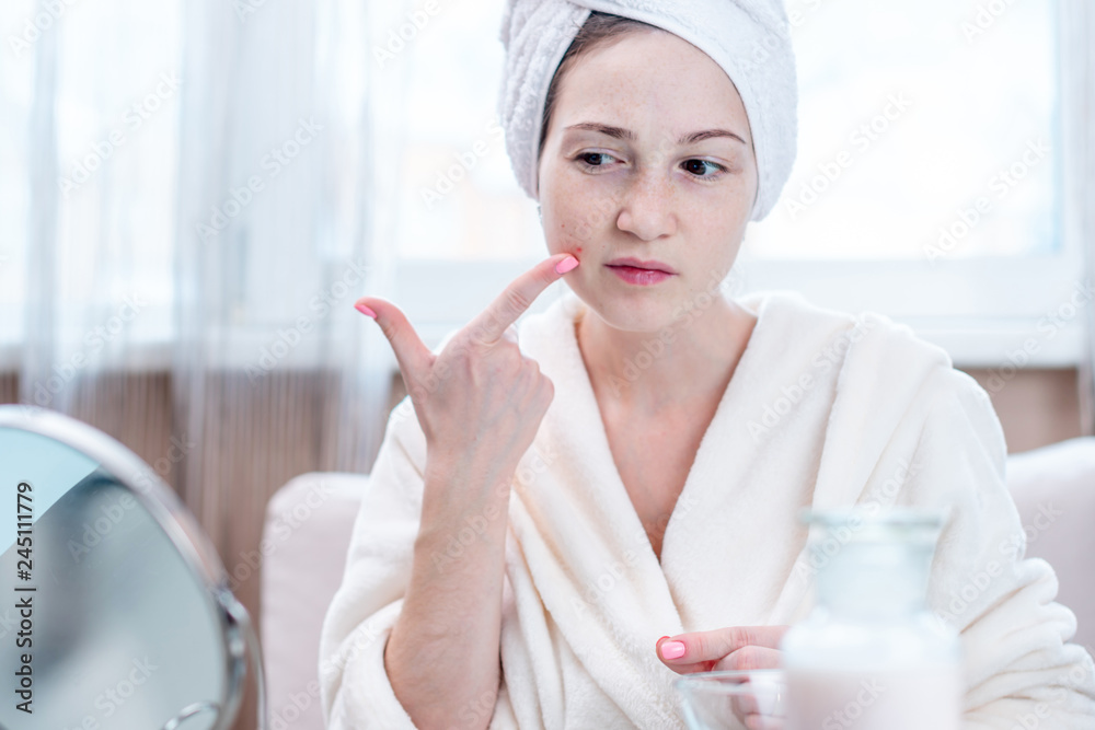 Beautiful unhappy young woman detects acne on her face. Concept of hygiene and care for the skin Beautiful unhappy young woman detects acne on her face. Concept of hygiene and care for the skin