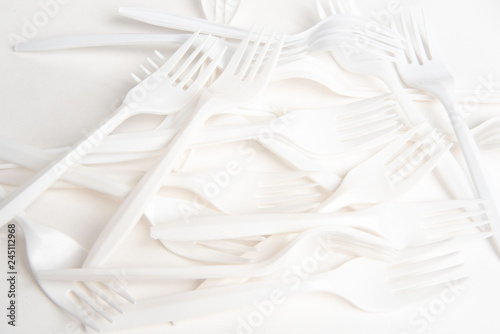 A bunch of disposable single-use white plastic forks set on a seamless white paper background.