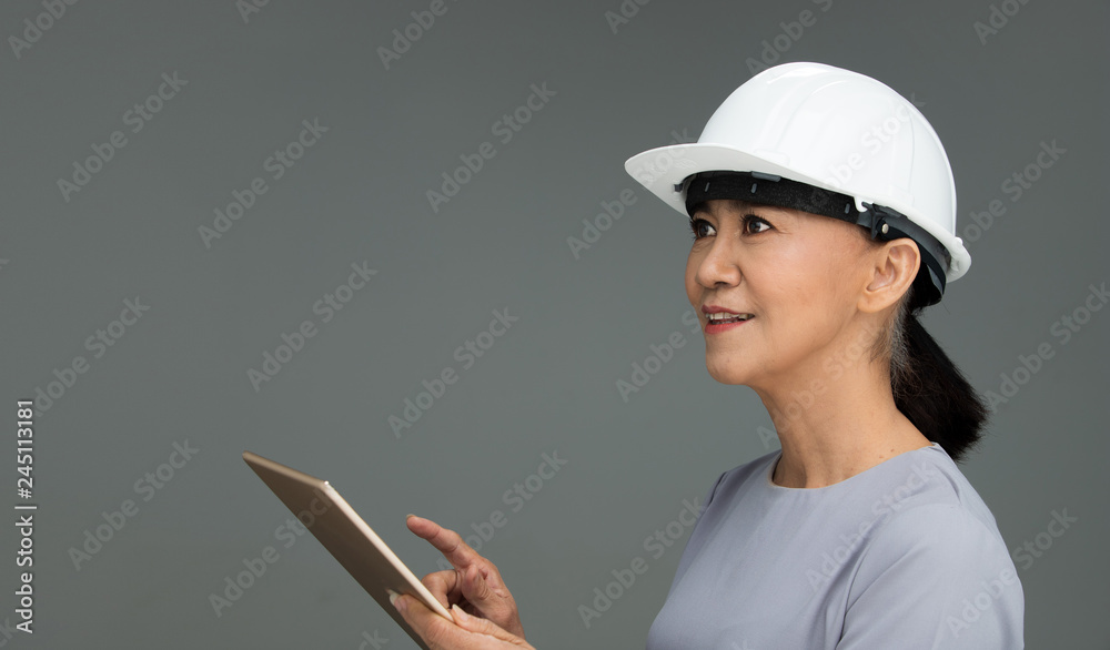 Beautiful Asian Smart Architect Engineer 50s 60s years old woman in white hard hat helmet hold tablet iot, portrait studio lighting gray background copy space, concept aging society woman can do Beautiful Asian Smart Architect Engineer 50s 60s years old woman in white hard hat helmet hold tablet iot, portrait studio lighting gray background copy space, concept aging society woman can do