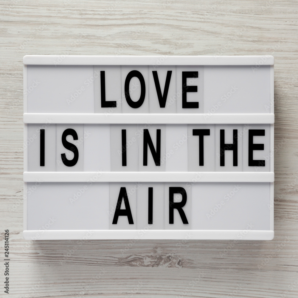 Modern board with text 'Love is in the air' on a white wooden surface. Valentine's Day 14 February. Modern board with text 'Love is in the air' on a white wooden surface. Valentine's Day 14 February.
