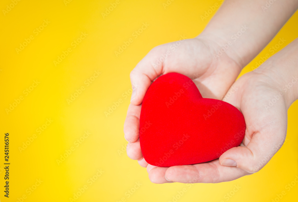 a red heart is holding in hands on yellow