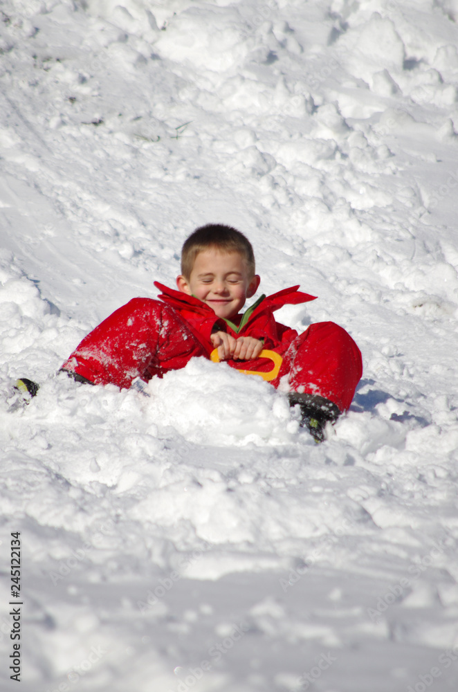 vacances d'hiver - enfant en combinaison rouge faisant de la luge