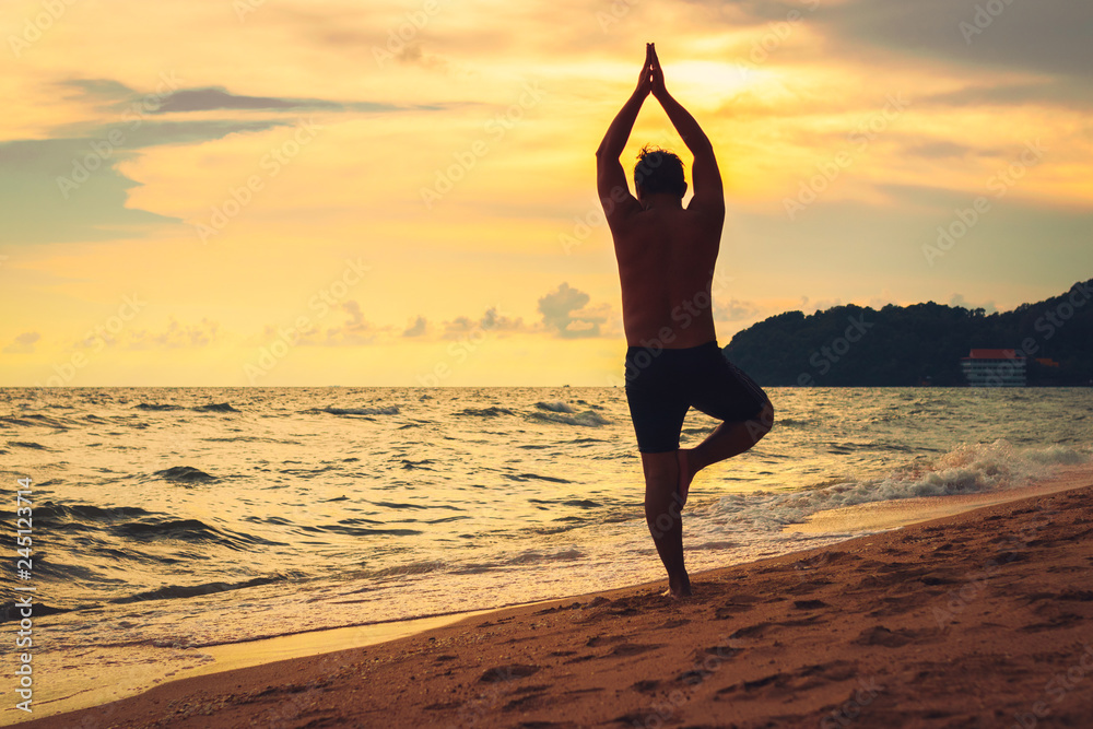 Beautiful silhouette of man practicing yoga on the beach at sunset.
