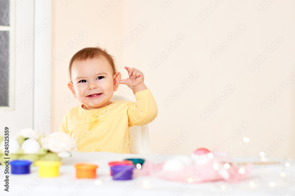 Baby girl sitting at the table and painting holiday easter eggs smiling happy childhood concept Baby girl sitting at the table and painting holiday easter eggs smiling happy childhood concept