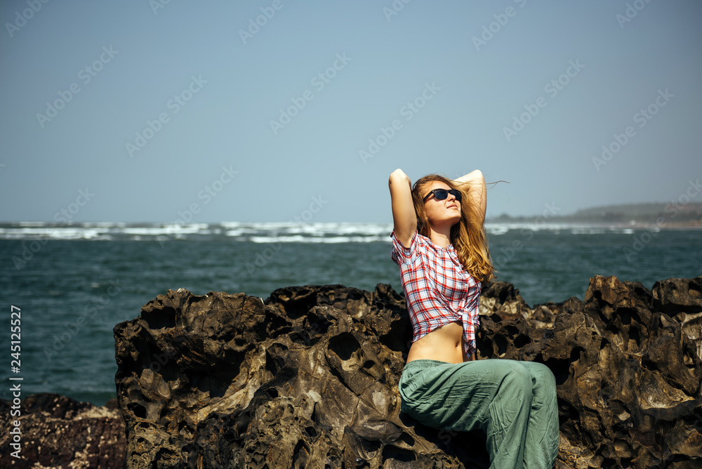 Beautiful girl in sunglasses relaxing on sea rocks Beautiful girl in sunglasses relaxing on sea rocks