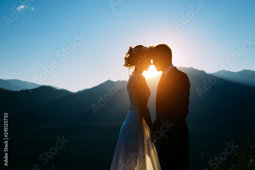 Happy wedding couple staying over the beautiful landscape with mountains during sunset