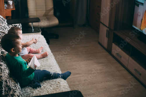 little girl and brother with remote on the couch watching TV on their own