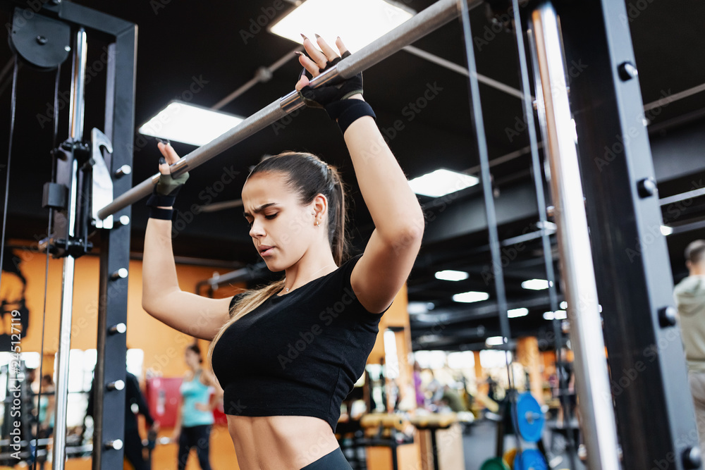 strong-willed young female fitness model engaged with a barbell in the Smith simulator in the gym. Concept of strong muscles and taut figure strong-willed young female fitness model engaged with a barbell in the Smith simulator in the gym. Concept of strong muscles and taut figure