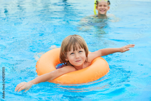 Cute little boy swimming in pool with inflatable ring on summer vacation