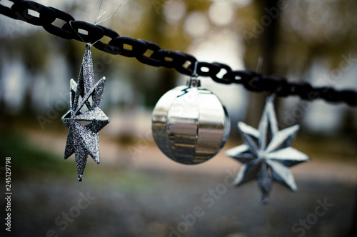 Decoraciones de navidad compuesta por dos estrellas y una bola de árbol de navidad en colores plateados en una cadena en el parque con tonos fríos photo