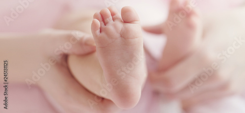 Closeup of mother hands holding cute tiny baby feet, showing baby foot. Pink Background. Horizontal. © nerudol