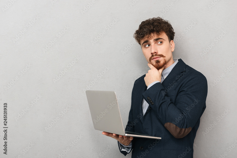 Handsome young business man isolated over grey wall background using laptop computer. Handsome young business man isolated over grey wall background using laptop computer.