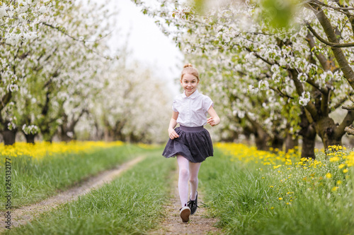 Little blonde girl running in blooming apple and cherry garden. Warm springtime and mothers and woman day