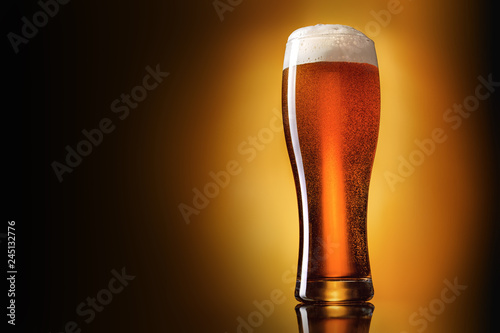 Glass of classic lager beer on gradient yellow to brown background. Studio shot.