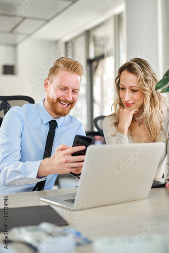 Two colleagues working in office, he is showing something to her on his smartphone