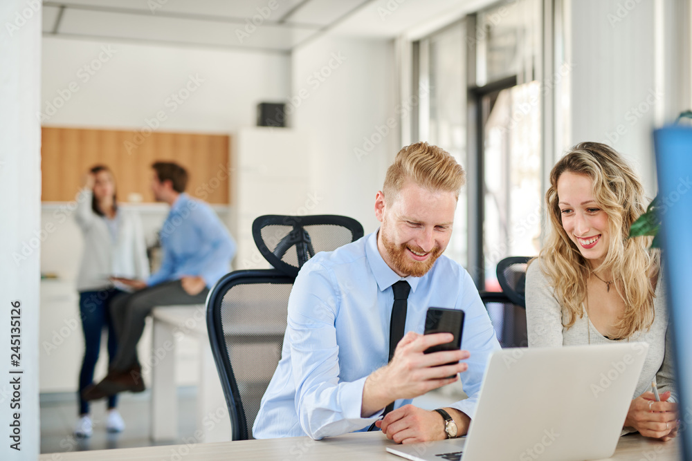 Obraz premium Two colleagues working in office, he is showing something to her on his smartphone