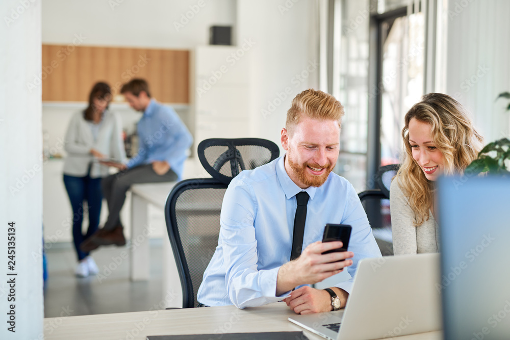 Two colleagues working in office, he is showing something to her on his smartphone