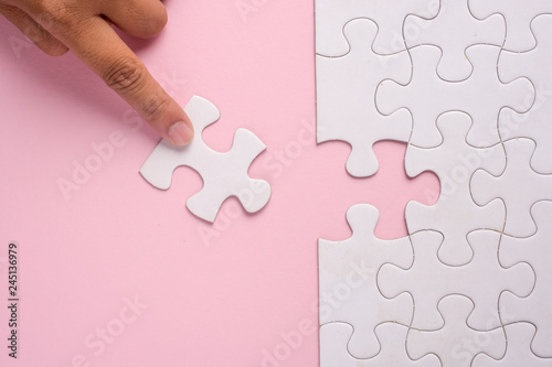 Foto Close up of hand placing the last jigsaw puzzle piece on pink background