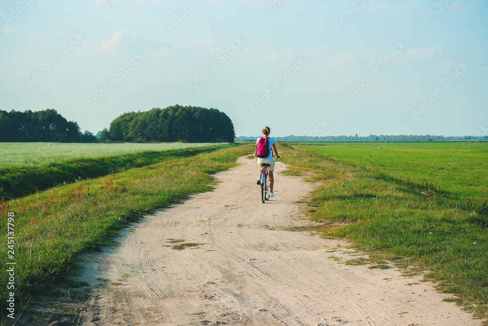 Young beautiful woman rides on a bicycle in the summertime on the green fields background