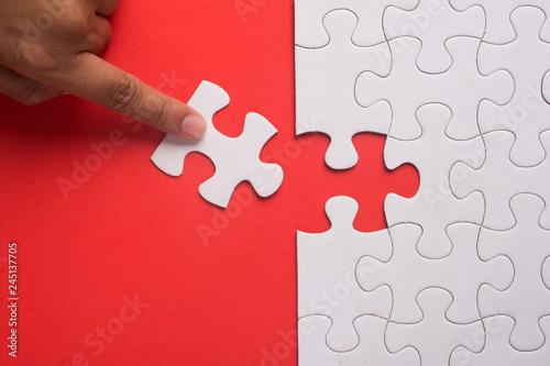 Close up of hand placing the last jigsaw puzzle piece on red background. Business and team work concept.