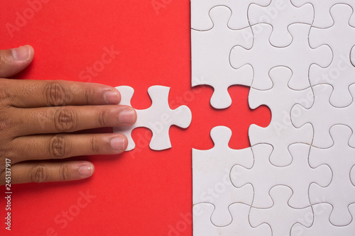 Fotografie Close up of hand placing the last jigsaw puzzle piece on red background