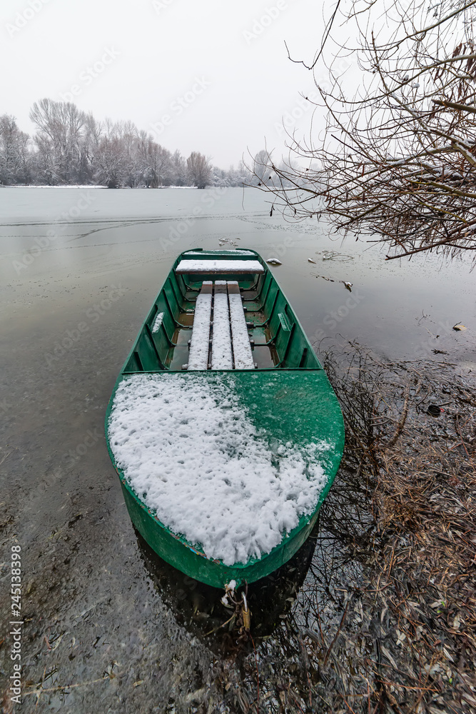 Naklejka premium Danube island (Šodroš) near Novi Sad, Serbia. Colorful landscape with snowy trees, beautiful frozen river. A boat covered with snow.