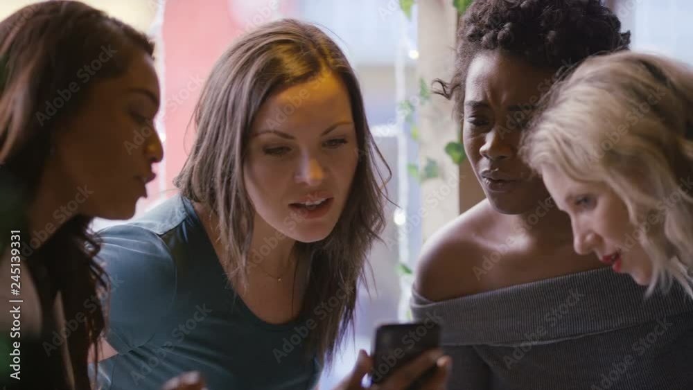 Female friends gathered around a cell phone in a coffee shop