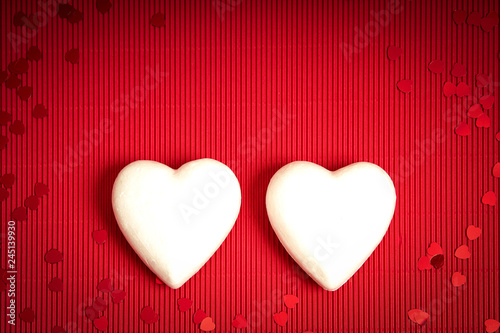 Valentines Day background with red ribbed paper with two white styrofoam hearts for lovers