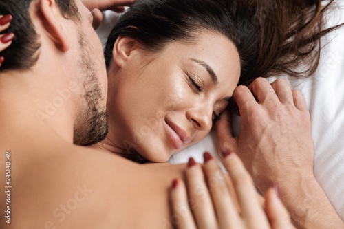 Photo of satisfied couple man and woman hugging together, while lying in bed at home or hotel apartment