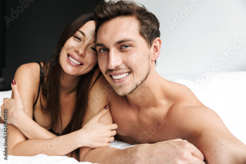 Beloved couple man and woman hugging together, while lying in bed at home or hotel apartment