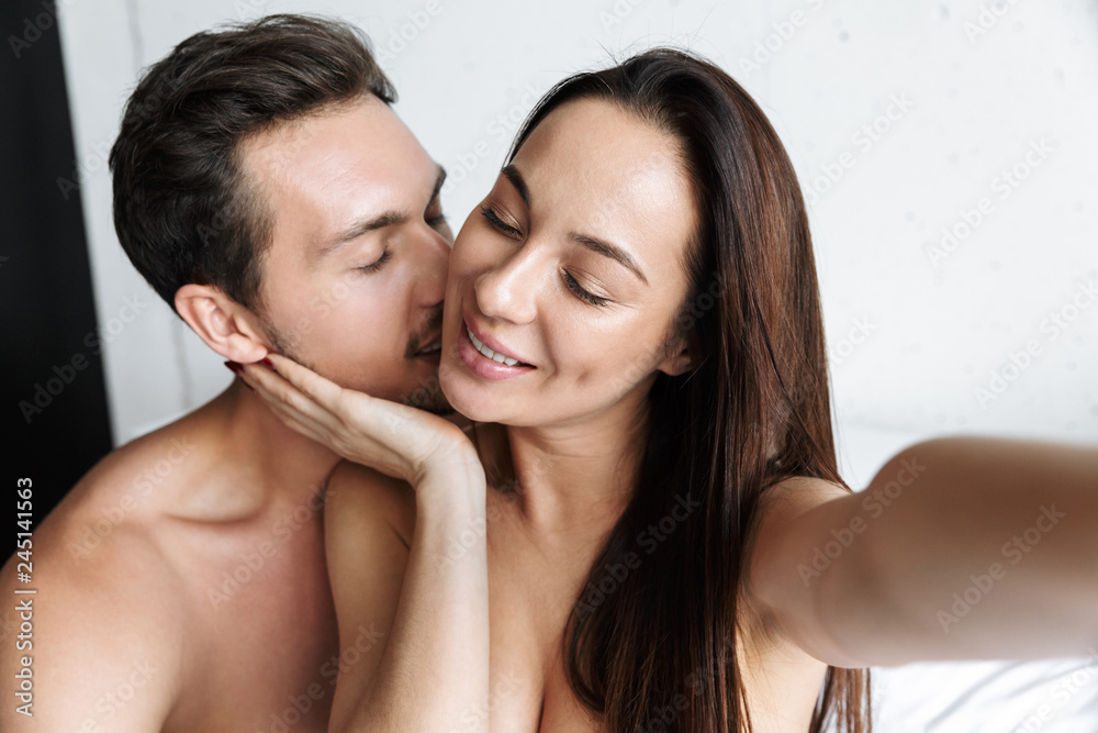 Image of smiling couple man and woman taking selfie photo together, while lying in bed at home or hotel apartment Image of smiling couple man and woman taking selfie photo together, while lying in bed at home or hotel apartment