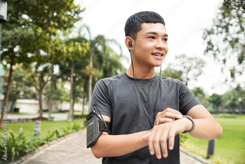 Cheerful Vietnamese man setting fitness tracker before jogging outdoors in the morning