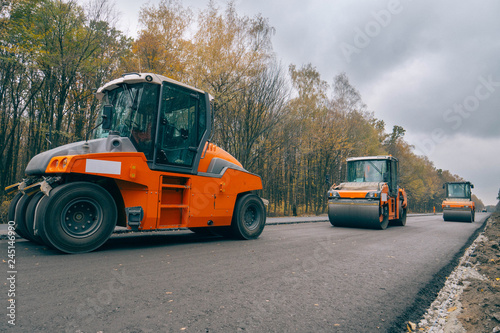 Road asphalt rollers are working on laying a new road on the background of yellow autumn forest