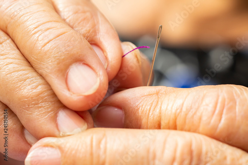 Senior woman's hands finishing to thread a needle, Purple colour roll of thread, Close up & Macro shot, Selective focus, Blurred and bokeh background, Tailor, Needlework concept