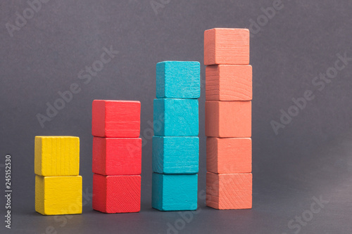 Toy wooden blocks as financial graph. Graph with four 4 steps. Growing chart. Infographic diagram, chart over grey or black or dark background. Multi-colored wooden blocks.