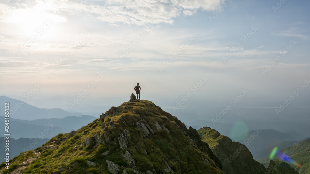 Young female hiker looking over the valley from the top of the mountain in the sunset