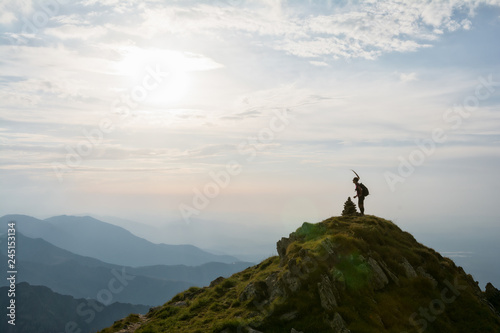 Young female hiker celebrating success on the top of the mountain in the sunset