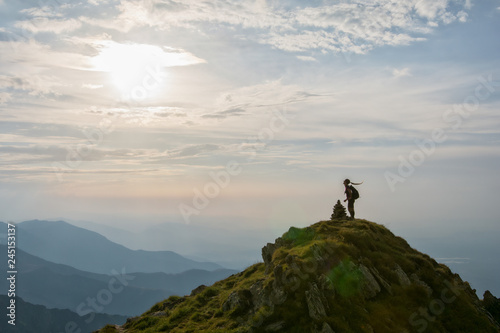 Young female hiker celebrating success on the top of the mountain in the sunset