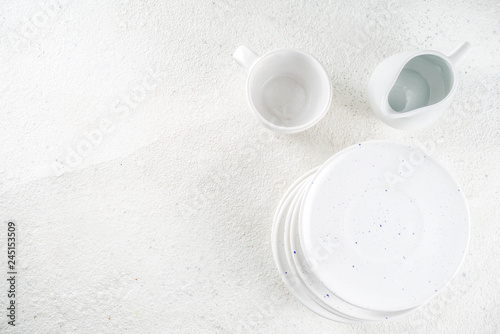 Assortment stack clean empty new white kitchen utensils  plates  bowls  cups mugs. On a white concrete background