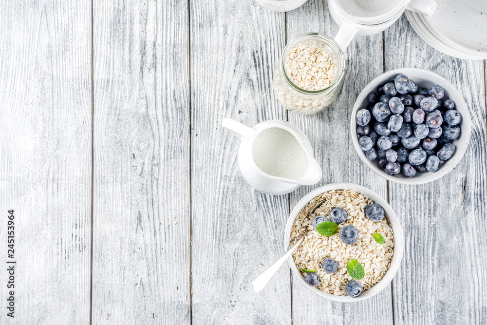 Healthy cereal and milk breakfast concept, dry oats in small bowl, with milk and fresh blueberry, white  wooden concrete background copy space
