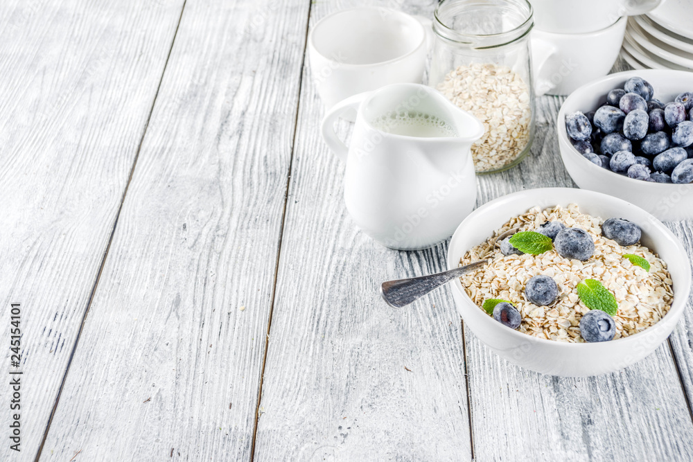 Healthy cereal and milk breakfast concept, dry oats in small bowl, with milk and fresh blueberry, white wooden concrete background copy space Healthy cereal and milk breakfast concept, dry oats in small bowl, with milk and fresh blueberry, white wooden concrete background copy space