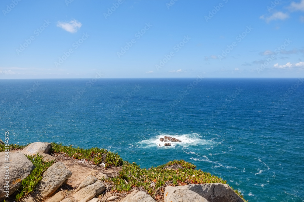 Deep blue water of calm Atlantic Ocean with small waves hitting rocks. Cape Cabo da Roca in Sintra. Lisbon, Portugal.