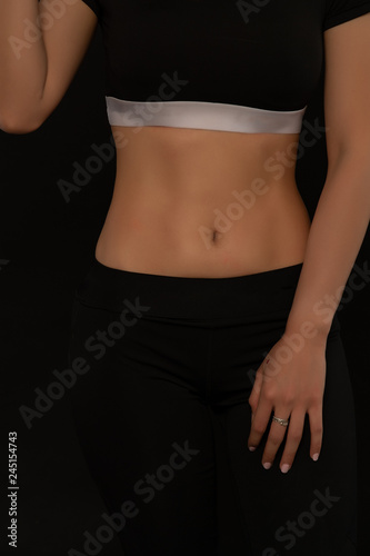 Slim and sexy stomach of woman on black background; sporty female girl showing her perfect body.
